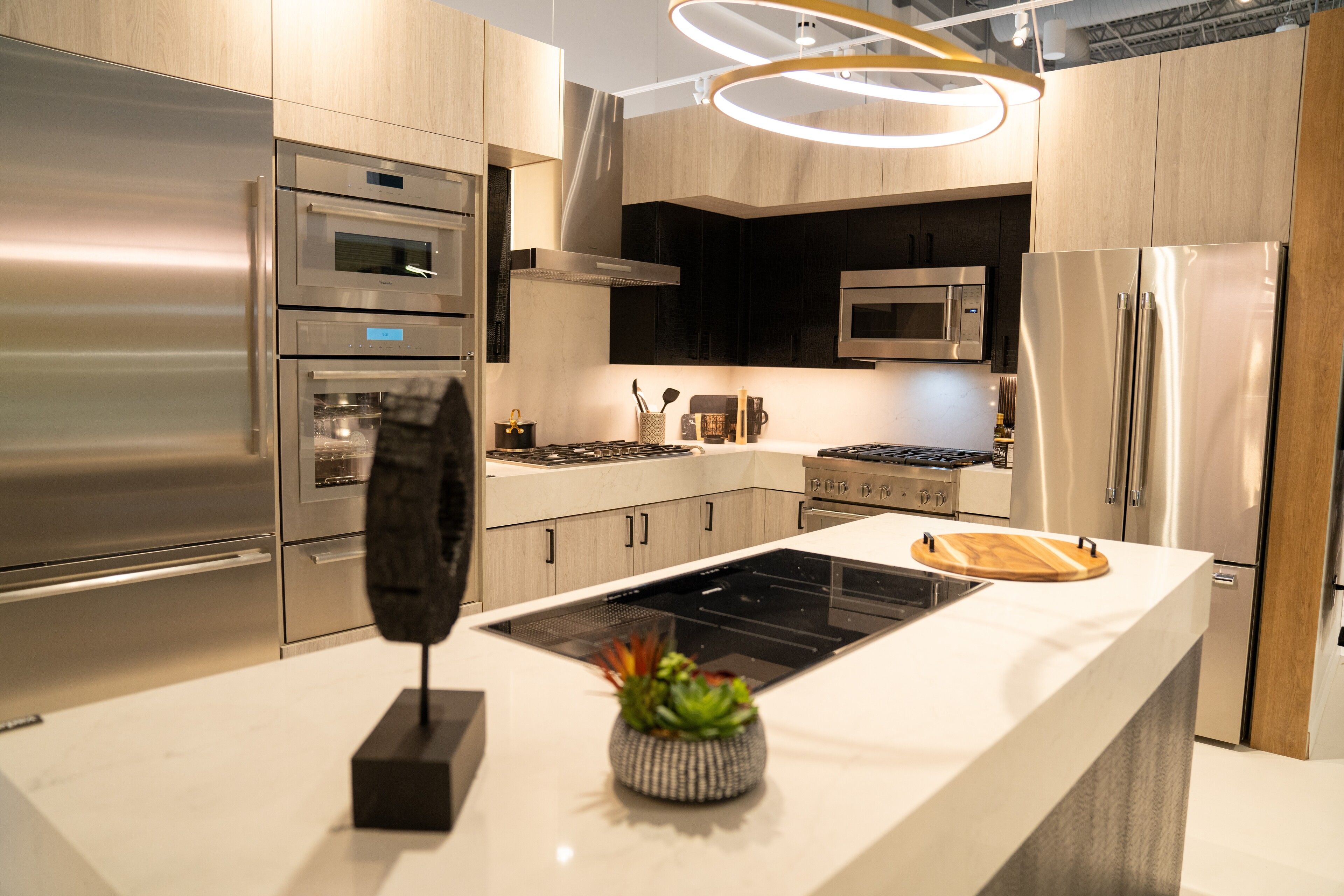 Greige cabinetry with a dark waterfall island beneath a ring pendant